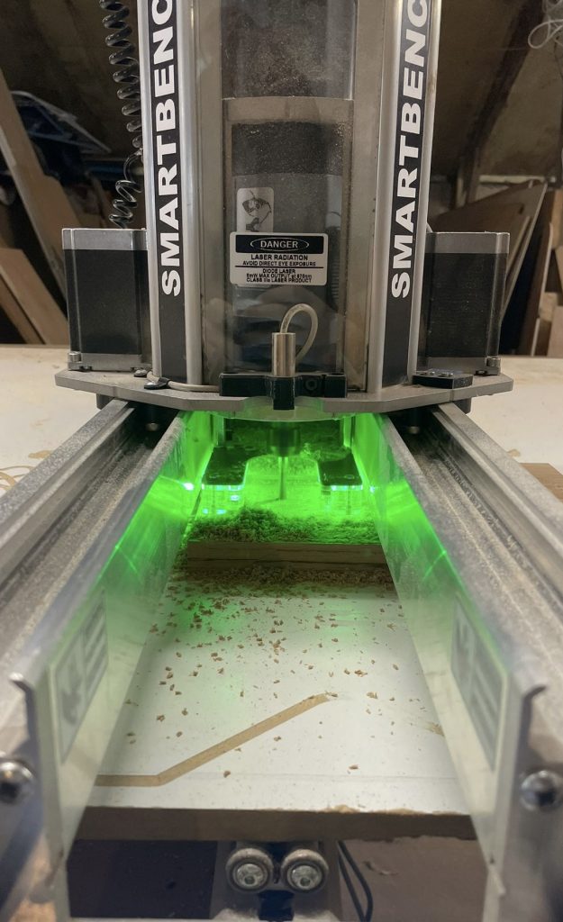 CNC router machine cutting into wood under green lights — precision CNC machining in Cambridgeshire.