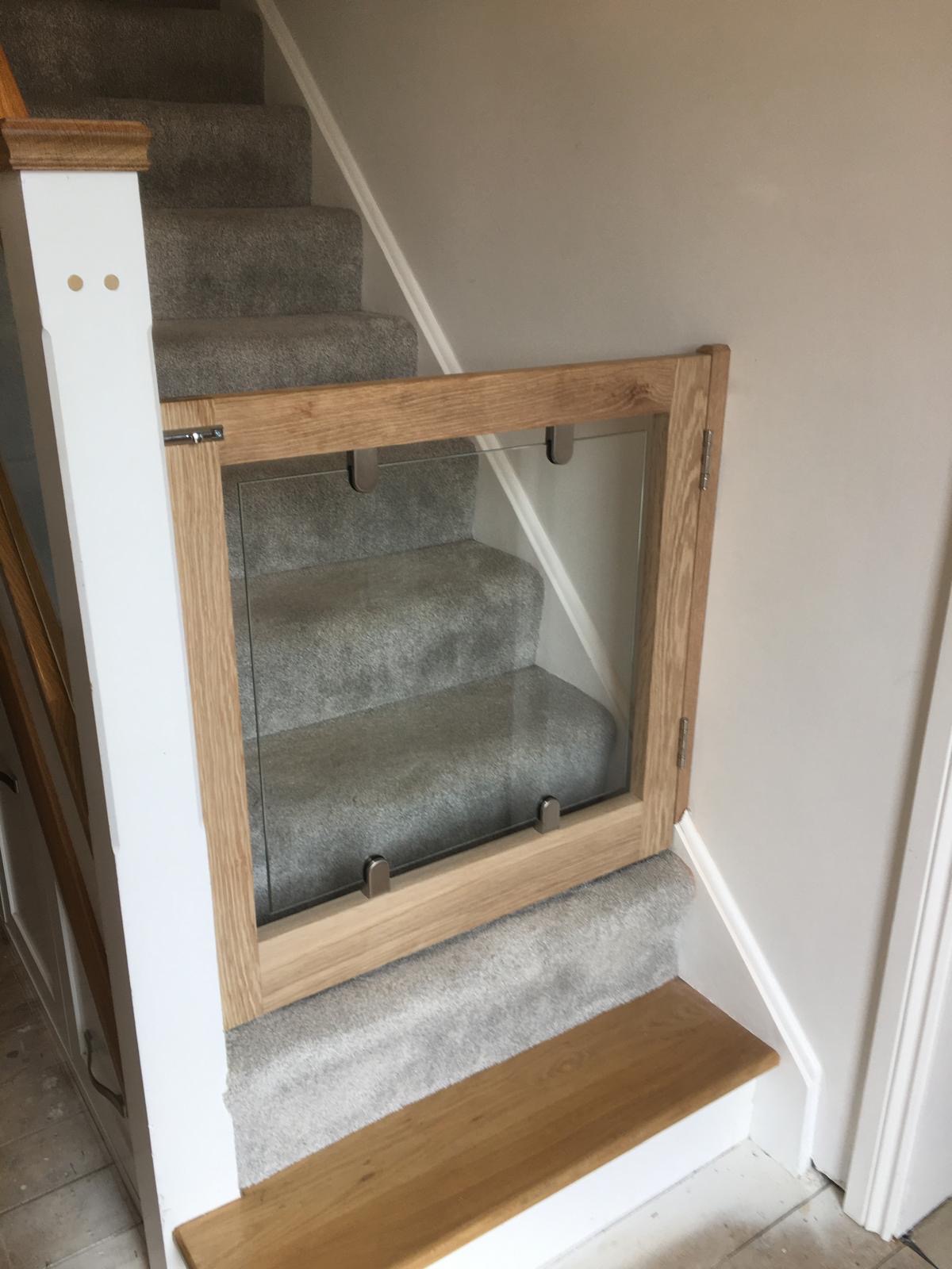 Oak and glass dog gate with brushed metal fixtures installed in hallway — bespoke carpentry detail.