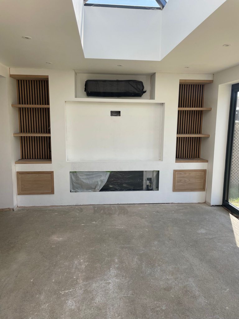 Custom media wall joinery with oak cabinetry being installed on each side of the TV recess — handcrafted in Cambridgeshire.