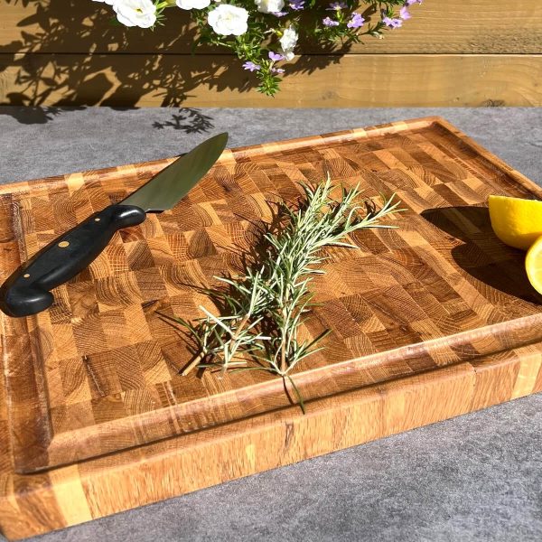 Angled view of a personalised oak end grain chopping board with knife, rosemary and lemon outdoors.