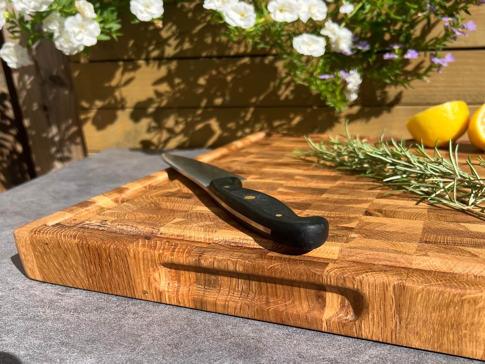 Close-up of a handmade oak end grain chopping board with side handles, knife, rosemary and lemon.