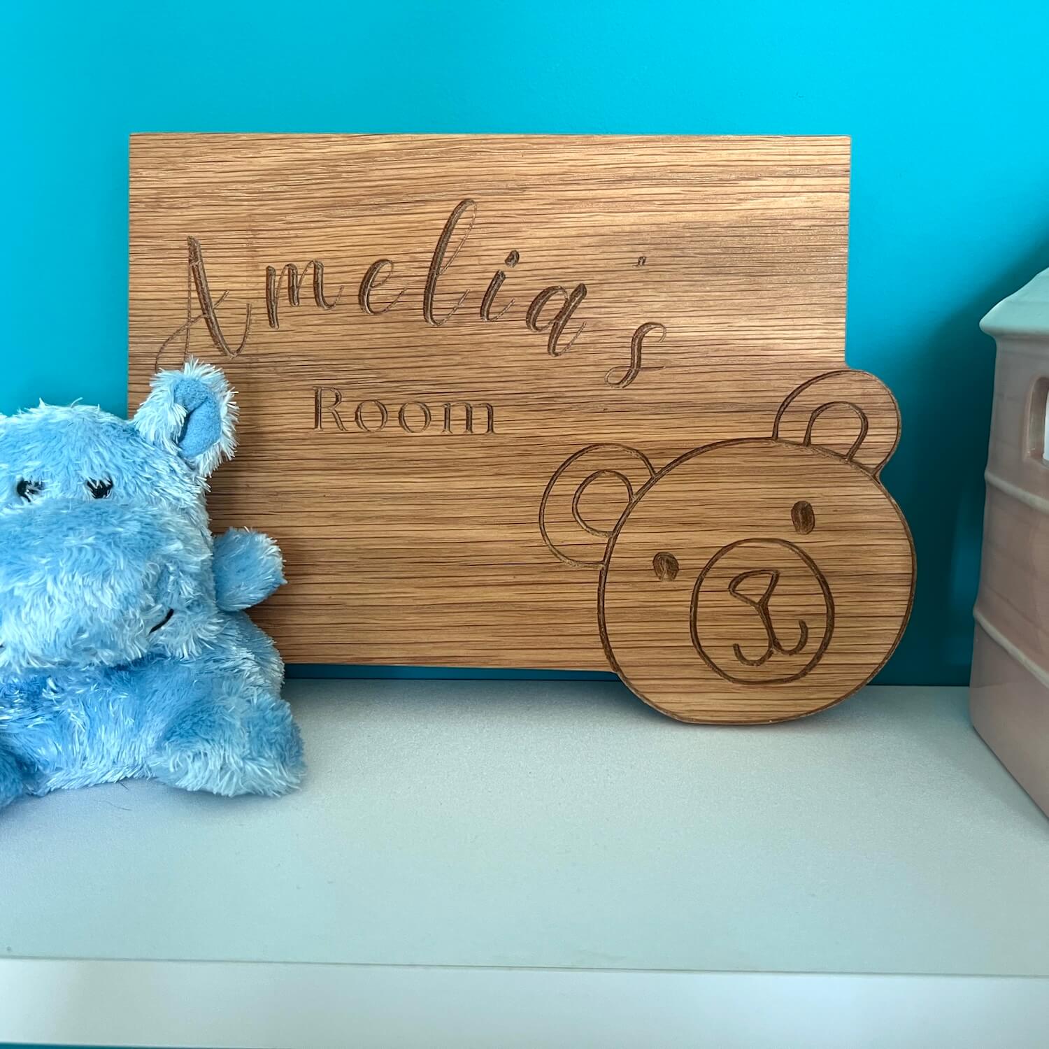 Close-up of a personalised oak children’s nursery sign with teddy bear engraving, styled with toys.