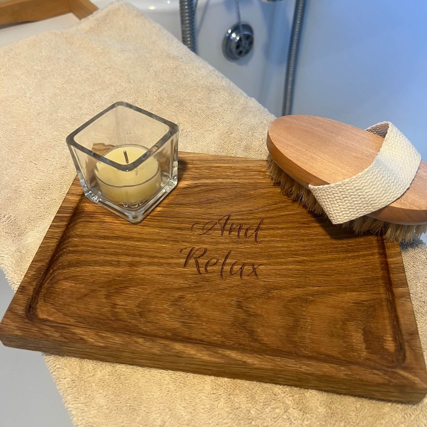 Oak display and storage tray engraved with “And Relax,” styled with a candle and body brush.