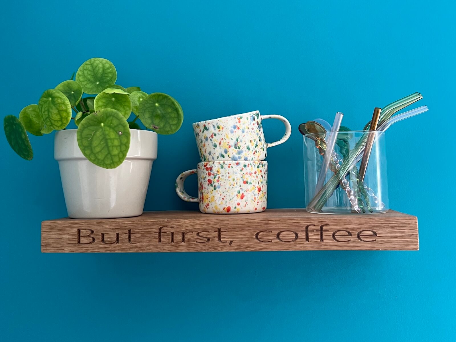 Personalised oak floating shelf engraved with “But first, coffee” styled with mugs and a plant.