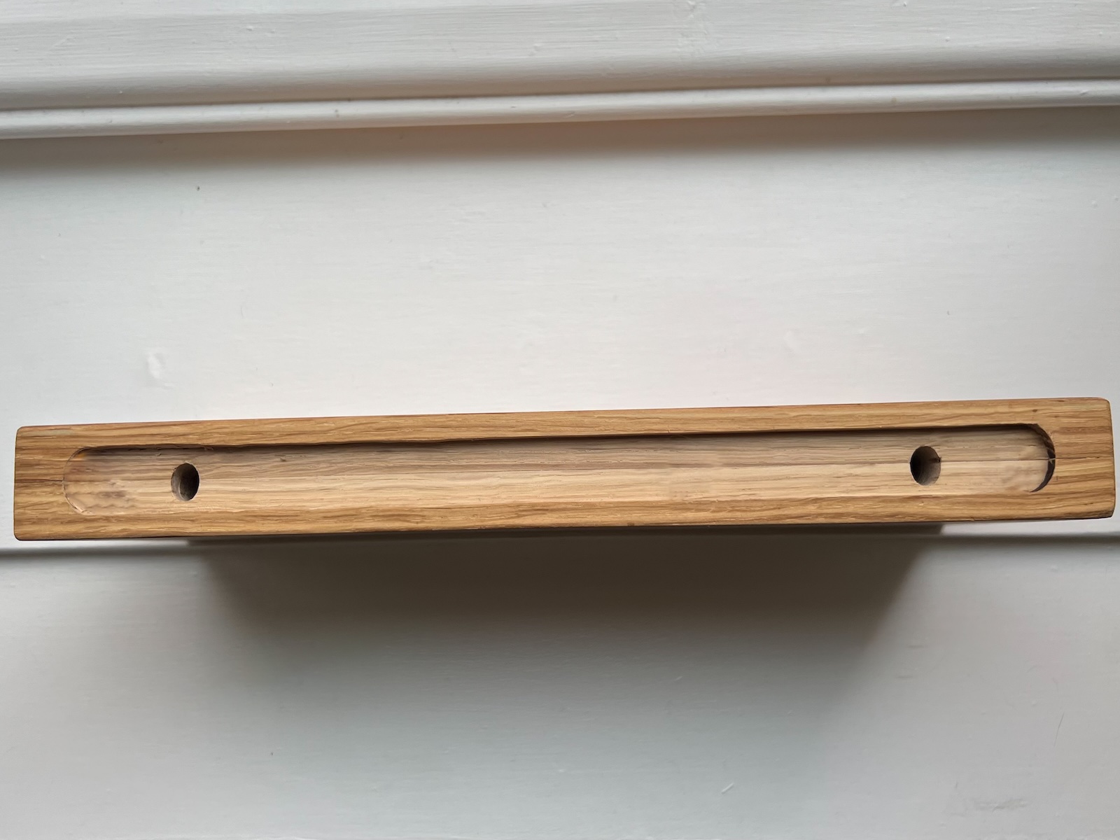 Underside view of oak floating shelf showing pre-drilled holes for concealed wall brackets.