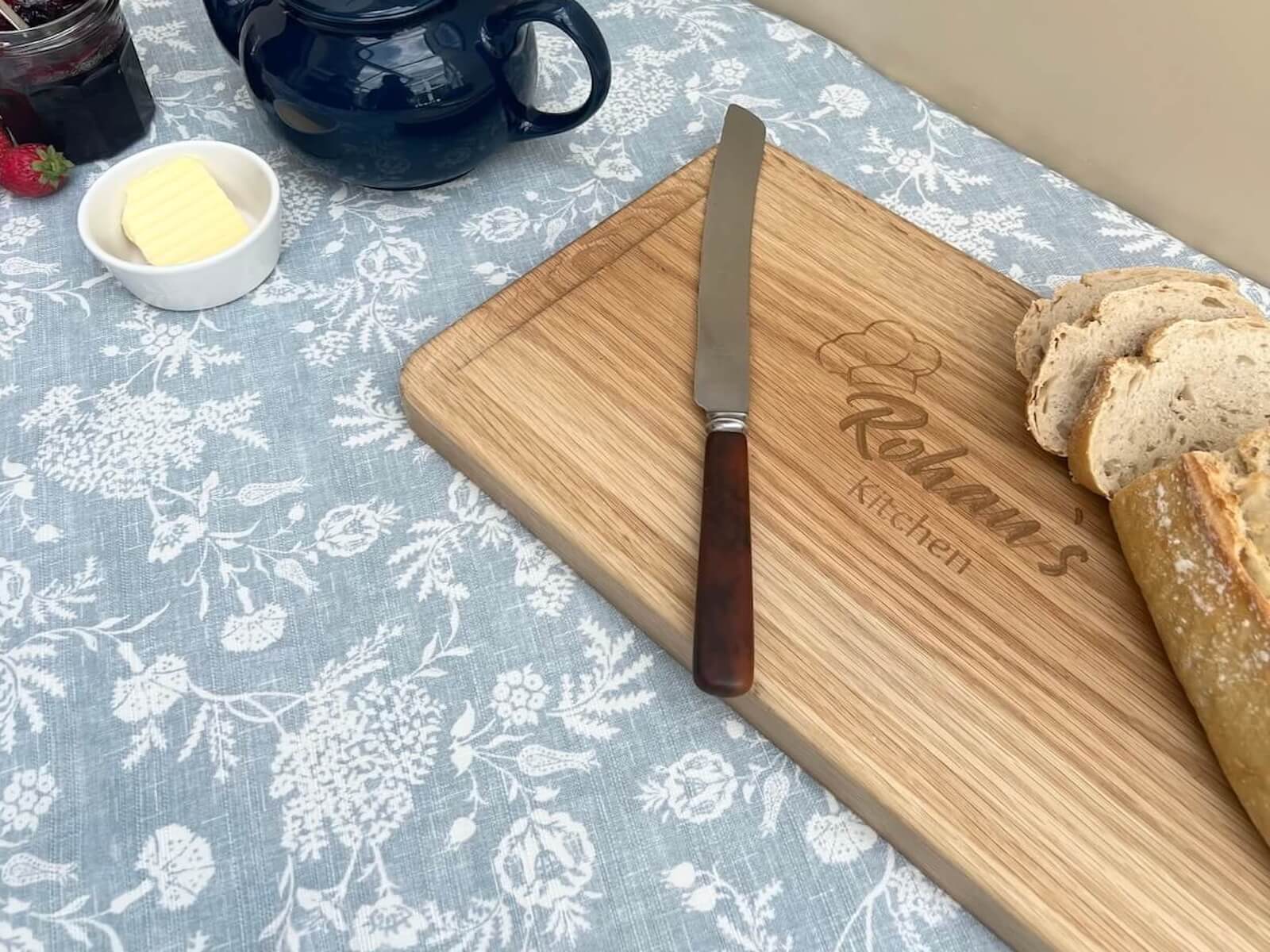 Personalised oak chopping board side view with tea set and bread.