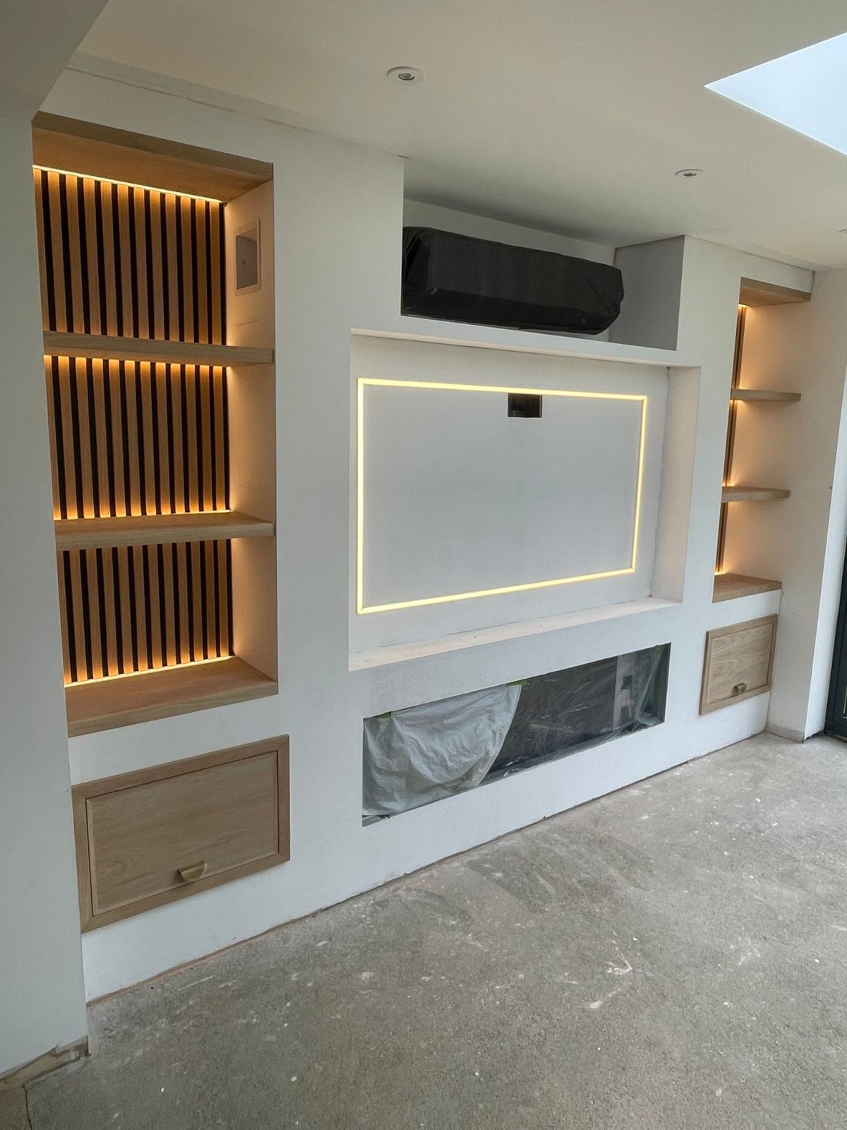 Solid oak shelving with integrated LED lighting and slatted panels on a bespoke media wall in Chatteris.