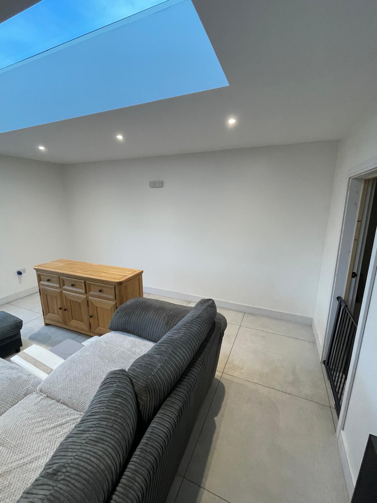 Plain living room with sofa and small cabinet before media wall installation Cambridgeshire.