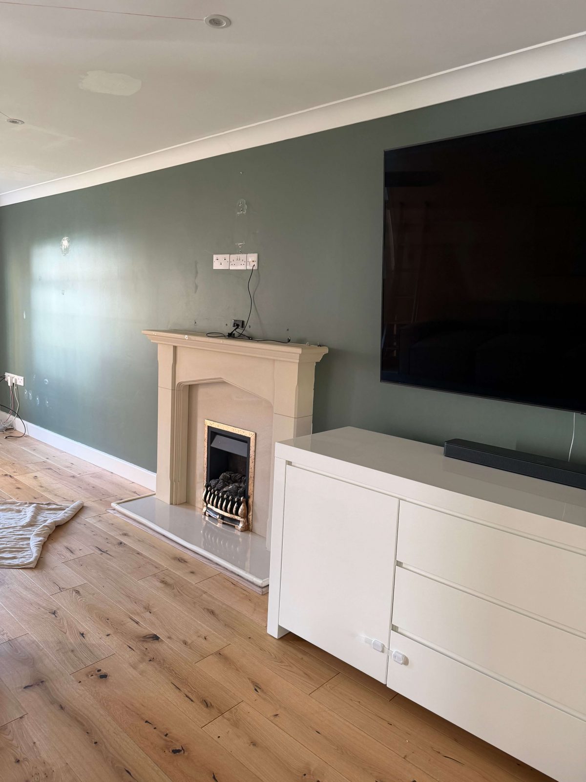 Living room with traditional fireplace and wall mounted TV before media wall installation Cambridgeshire.