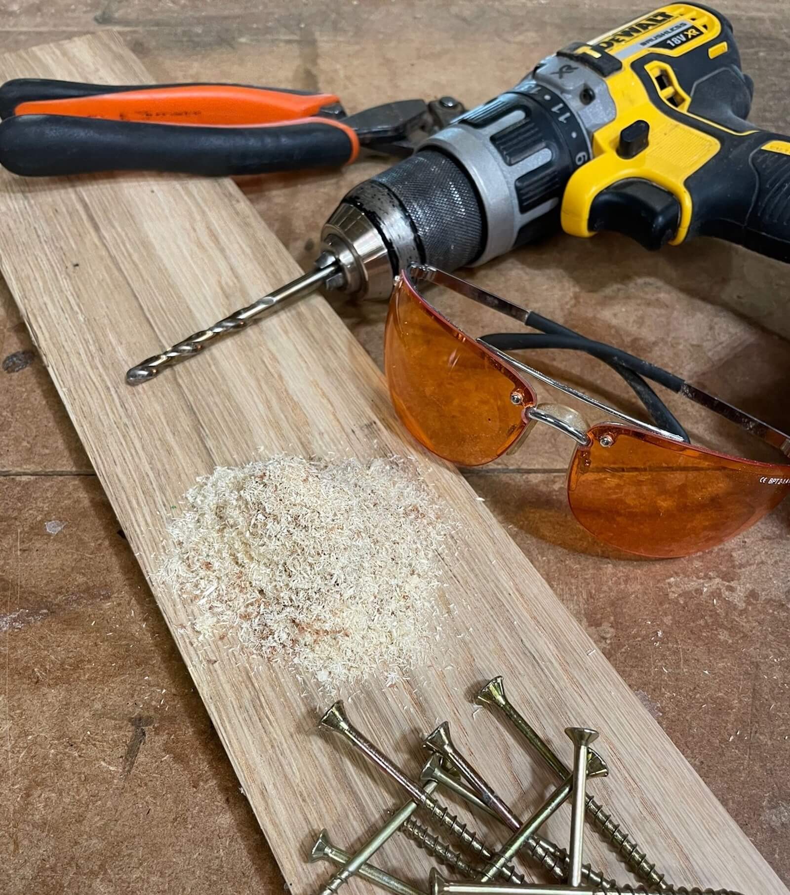 DeWalt drill, safety glasses and screws arranged on a wooden board with sawdust — workshop tools used by KMP Carpentry & Joinery in Cambridgeshire.
