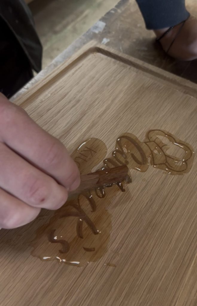 Levelling clear food-safe resin into the engraved design of a personalised oak chopping board to create a smooth, durable finish.