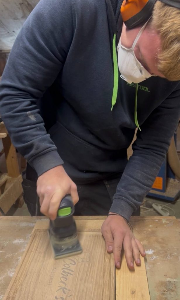 A woodworker sanding the engraved text on a personalised oak chopping board to refine the surface.