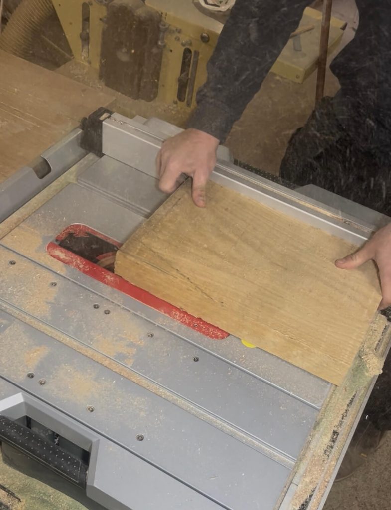 A woodworker using a table saw to shape a piece of white oak for a custom engraved chopping board.