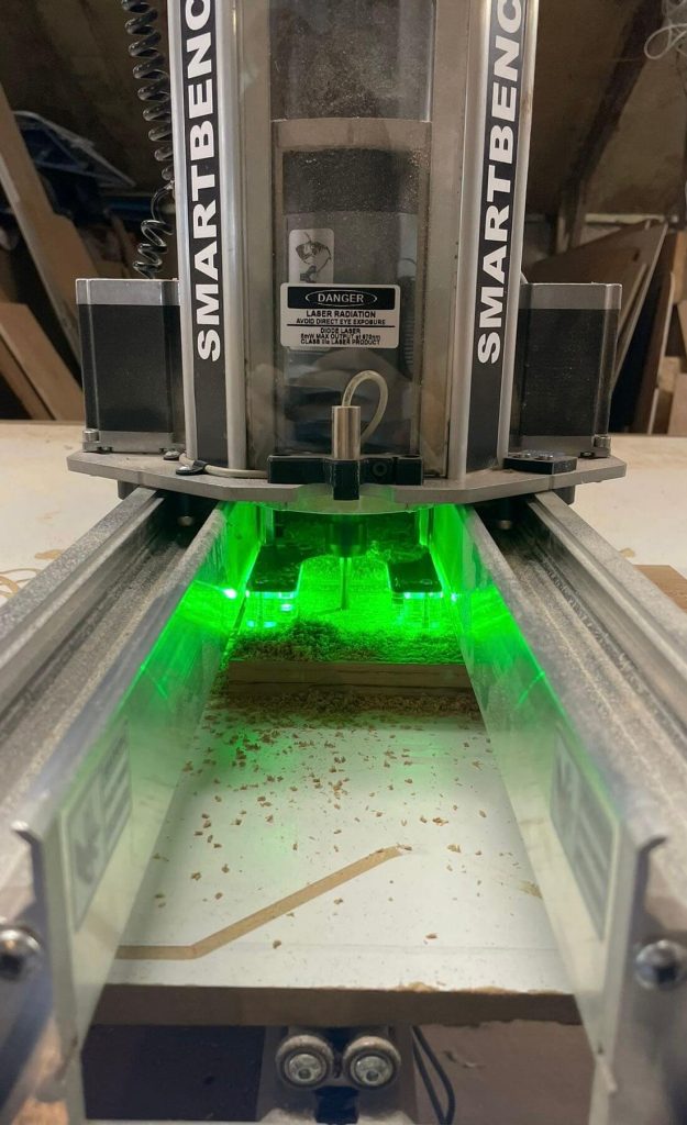 CNC router machine cutting into wood under green lights — precision CNC machining in Cambridgeshire.