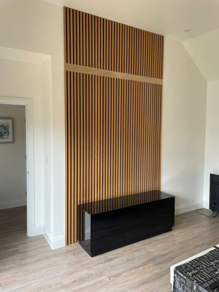 Bespoke oak slatted acoustic feature wall designed and installed in Cambridgeshire, showcasing modern joinery craftsmanship to enhance both style and sound within a living space.