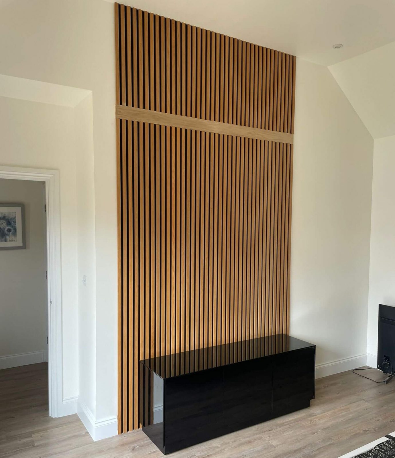 Oak slatted acoustic wall panels installed as a TV feature wall in a living room in Cambridgeshire.