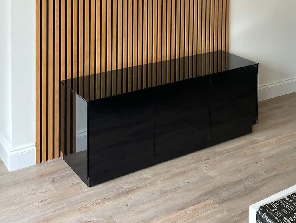 Oak slatted acoustic wall with custom black TV cabinet plinth, designed and installed as bespoke joinery in a St Neots living room.