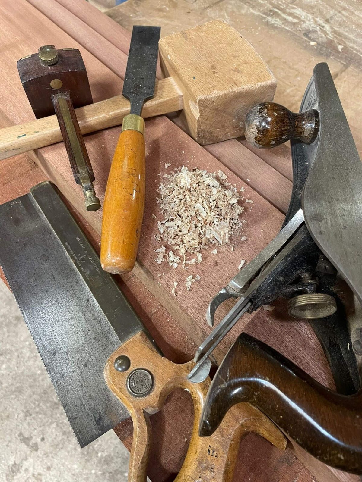 Traditional joinery hand tools including chisels, saw and mallet laid out on a wooden workbench.
