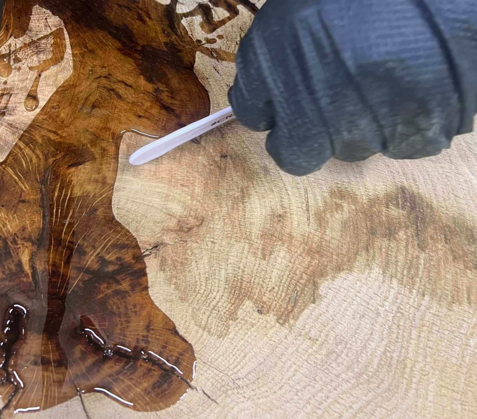 Applying clear epoxy resin to stabilise cracks in a customer supplied live edge oak slab before CNC engraving.