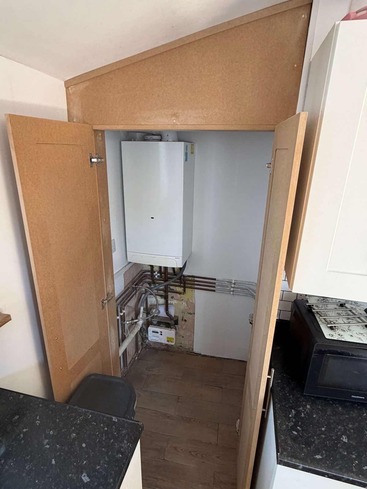 Fitted boiler housing cupboard open showing internal pipework and storage.