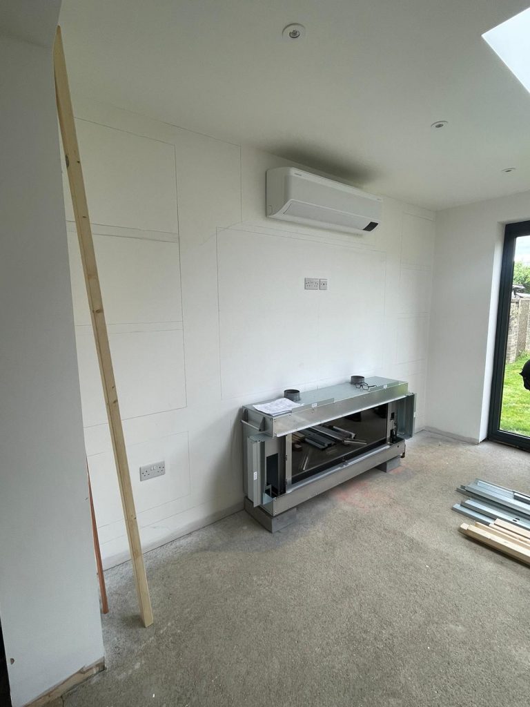 Before photo of a bespoke media wall project in Chatteris showing a blank wall with an existing air conditioning unit and fireplace.